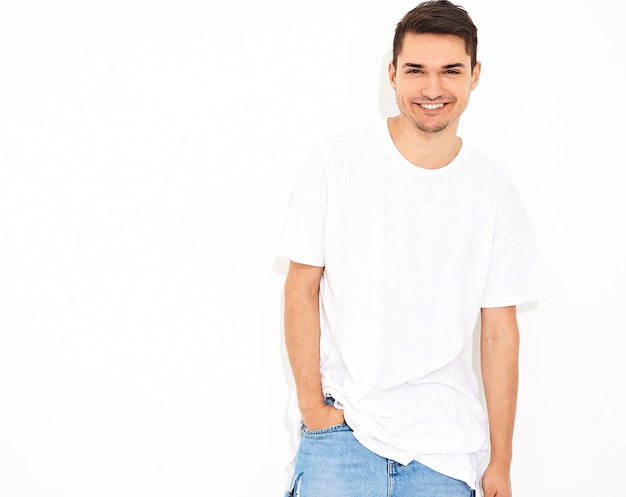 Portret van de knappe glimlachende jonge modelmens gekleed in jeanskleren en t-shirt het stellen. zijn hoofd aanraken