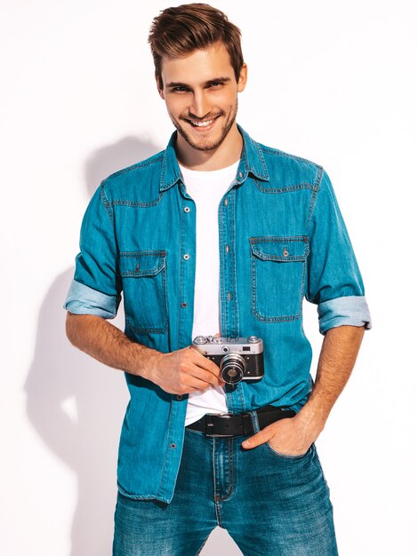 Portret van de knappe glimlachende mens die de kleren van de zomerjeans draagt. Model mannetje dat beeld op oude uitstekende fotocamera neemt.