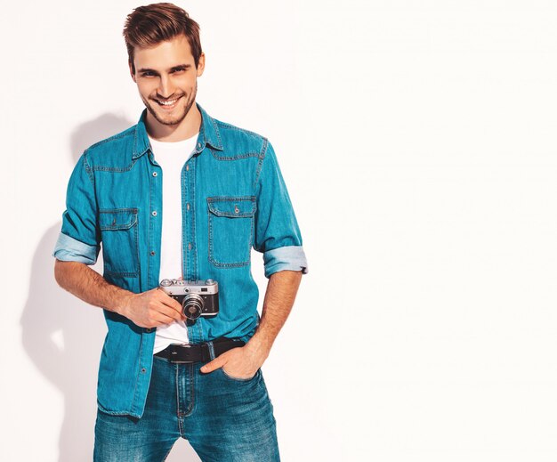 Portret van de knappe glimlachende mens die de kleren van de zomerjeans draagt. Model mannetje dat beeld op oude uitstekende fotocamera neemt.