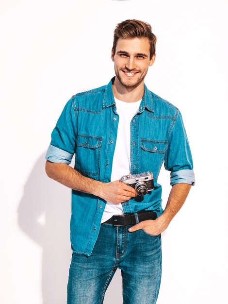 Portret van de knappe glimlachende mens die de kleren van de zomerjeans draagt. Model mannetje dat beeld op oude uitstekende fotocamera neemt.