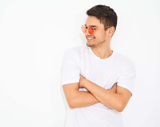 Portret van de knappe jonge modelmens gekleed in jeanskleren en T-shirt in zonnebril het stellen. Gekruiste armen