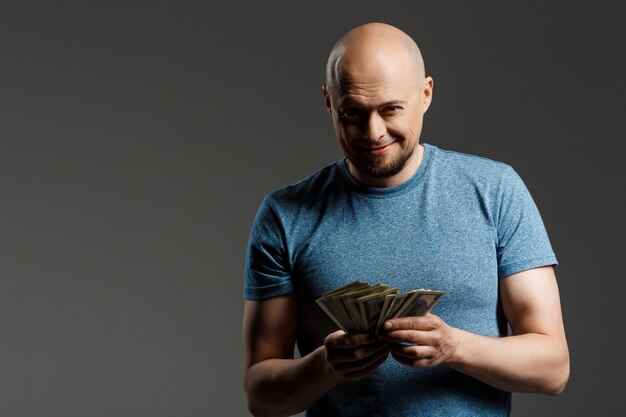 Portret van de knappe mens in het grijze geld van de overhemdsholding over donkere muur