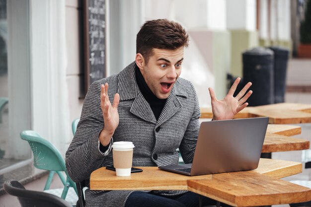 Portret van de verraste opgewonden mens die emotioneel in zilveren laptop kijkt, gilt en zich verheugt