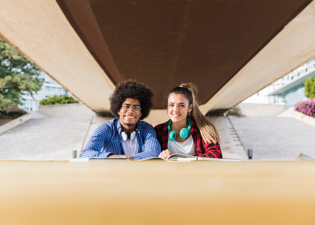 Portret van diverse jonge paarzitting onder de brug die samen bij universitaire campus bestuderen