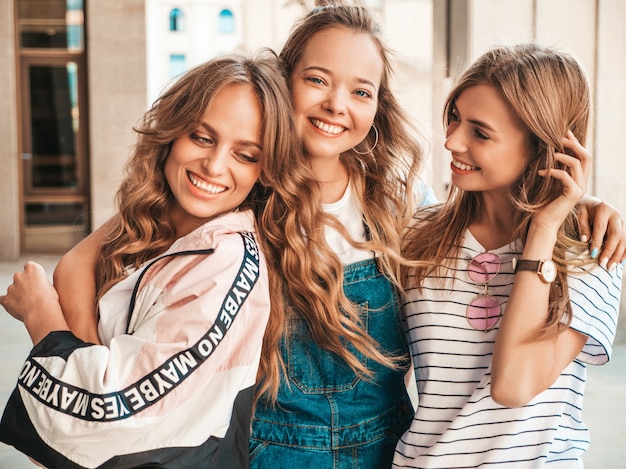 Gratis foto portret van drie jonge mooie glimlachende hipster meisjes in trendy zomerkleren. sexy zorgeloze vrouwen die zich voordeed op straat. positieve modellen met plezier