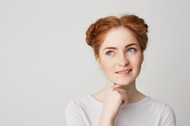 Portret van dromerige jonge mooie gember meisje denken dromen aanraken van kin glimlachend bijten lip.