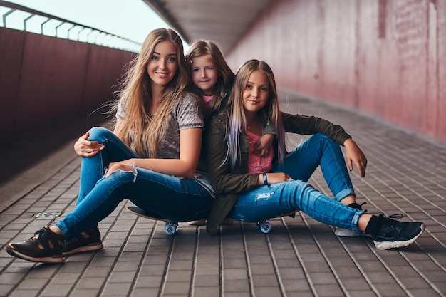 Portret van een aantrekkelijk gezin. Moeder en haar dochters zitten samen op een skateboard bij een brugvoetpad.