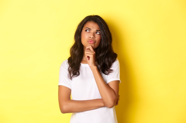 Portret van een aantrekkelijke Afro-Amerikaanse vrouw die denkt haar keuze te maken en naar de linkerbovenhoek te kijken...