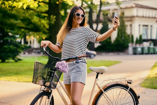 Portret van een aantrekkelijke brunette vrouw met een fiets in het stadspark.