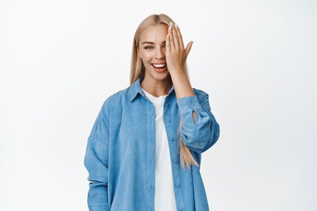 Portret van een aantrekkelijke glimlachende vrouw met blond haar en een witte glimlach, één kant van het gezicht naar beneden gericht en op wit kijkend