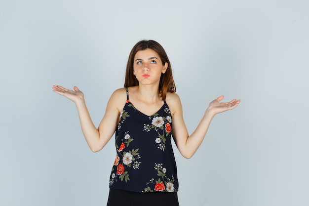 Portret van een aantrekkelijke jonge dame die een hulpeloos gebaar toont, op de wangen blaast in een blouse en er verward vooraanzicht uitziet