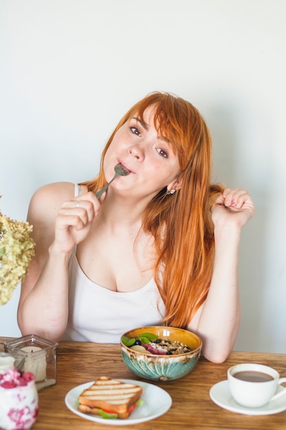 Gratis foto portret van een aantrekkelijke jonge vrouw die een lepel likt terwijl het hebben van ontbijt