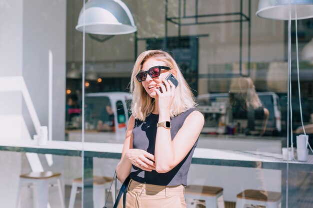 Portret van een aantrekkelijke jonge vrouw die zich voor winkel bevindt die op mobiele telefoon spreekt