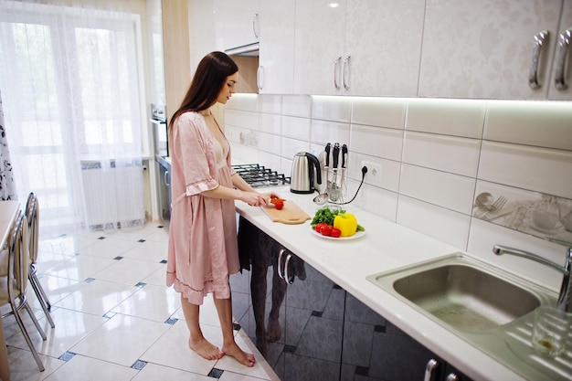 Portret van een aantrekkelijke jonge vrouw in gewaad die salade maakt van verse groenten in de keuken