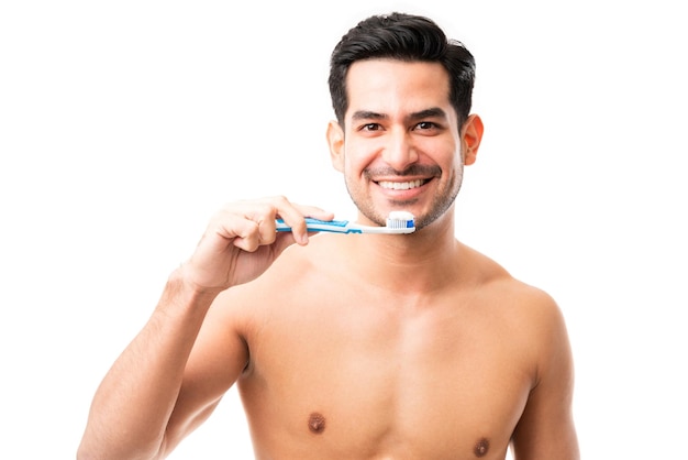 Portret van een aantrekkelijke man die een tandenborstel vasthoudt terwijl hij lacht in de studio