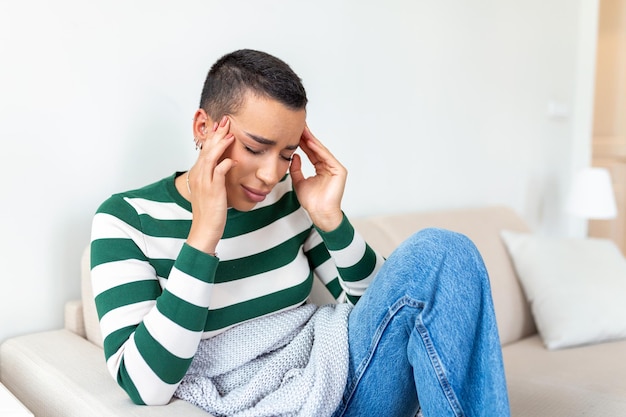 Gratis foto portret van een aantrekkelijke vrouw die thuis op een bank zit met hoofdpijn die pijn voelt en met een uitdrukking van onwel zijn verstoorde depressieve vrouw die op de bank ligt en sterke hoofdpijn voelt migraine