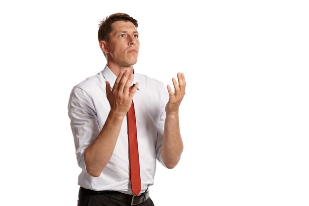 Portret van een aardige donkerbruine man met bruine ogen, gekleed in een wit overhemd en een rode stropdas. Hij bidt terwijl hij poseert in een studio geïsoleerd op een witte achtergrond. Concept van gebaren en oprechte emo