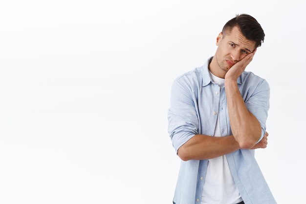 Portret van een aarzelende en vermoeide blanke man leunt op de handpalm en grimast terwijl hij wacht op het aankleden van zijn vriendin, humeurig en verdrietig, verdrietig omdat hij thuis in quarantaine zit