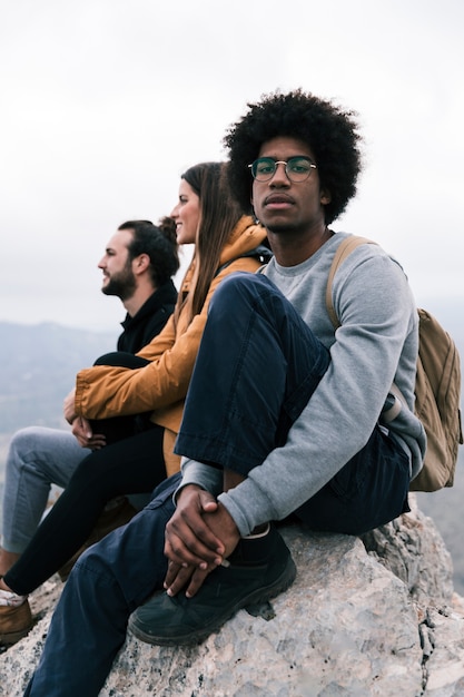 Portret van een Afrikaanse jonge man zittend op de bergtop met zijn vrienden camera kijken