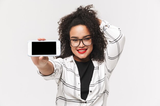 Portret van een afrikaanse vrouw staande geïsoleerd op een witte achtergrond, met een leeg scherm mobiele telefoon