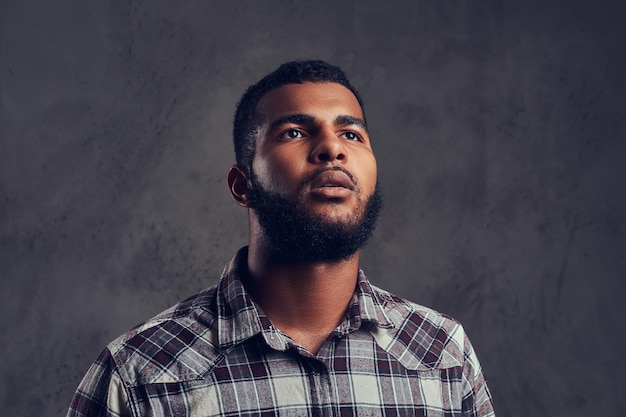 Portret van een Afro-Amerikaanse man met een baard die een geruit overhemd draagt op een donkere gestructureerde achtergrond.