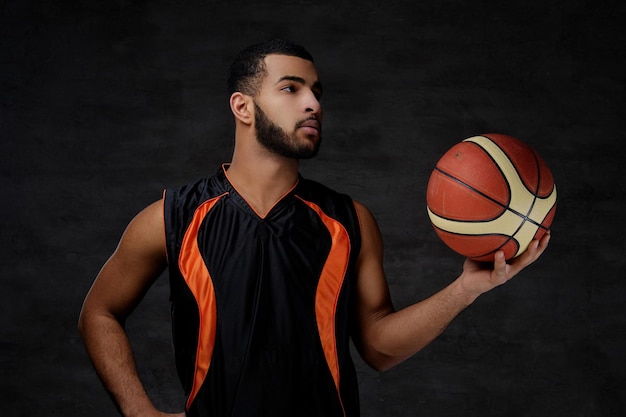 Portret van een Afro-Amerikaanse sportman. Basketbalspeler in sportkleding met een bal op een donkere achtergrond.