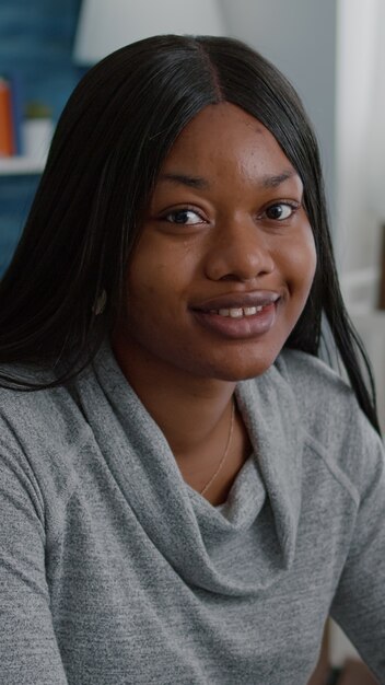 Portret van een Afro-Amerikaanse student die aan een bureautafel in de woonkamer zit en naar de camera kijkt