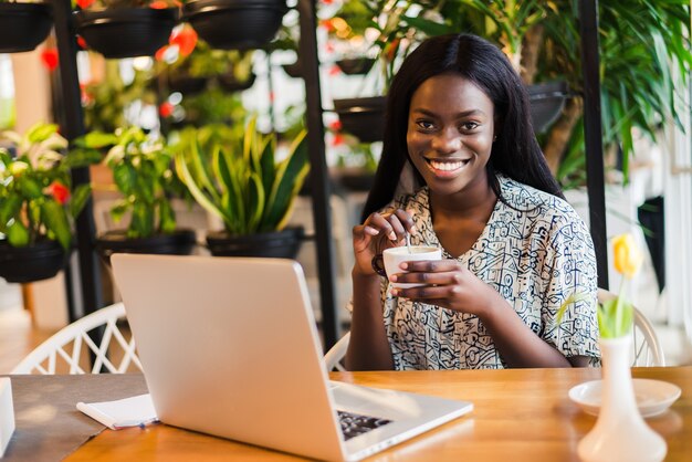 Portret van een Afro-Amerikaanse vrouw ontspannen in café met laptop en koffie