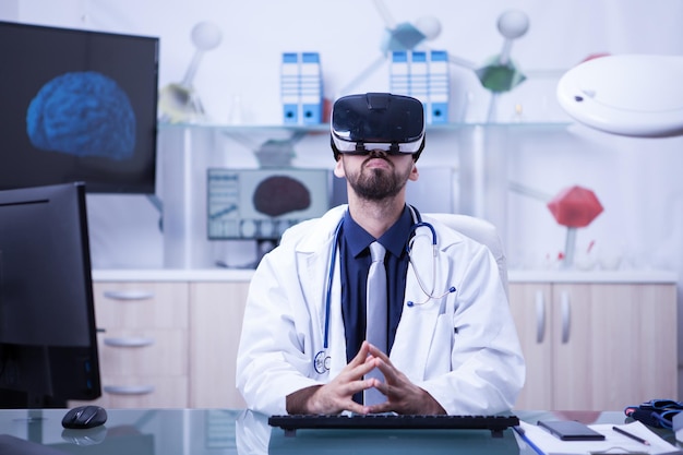 Portret van een arts die aan zijn bureau zit met behulp van virtual reality-hoofd dat omhoog kijkt. arts met behulp van moderne technologie.