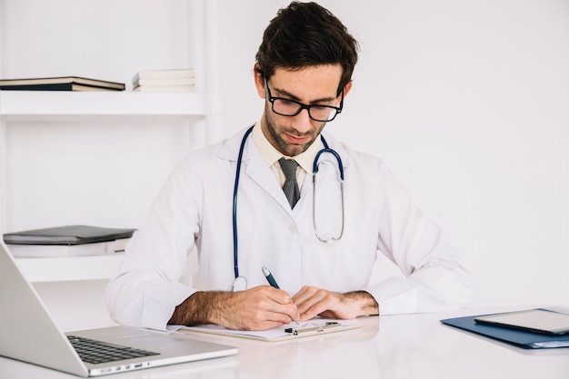 Portret van een arts die op klembord in kliniek schrijft