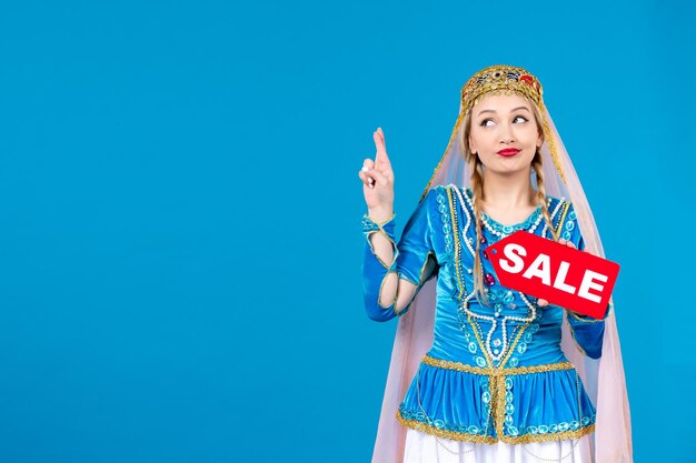 Portret van een azeri-vrouw in traditionele kleding met een rood verkoopnaambordje op een blauwe achtergrond, lente etnisch winkelen