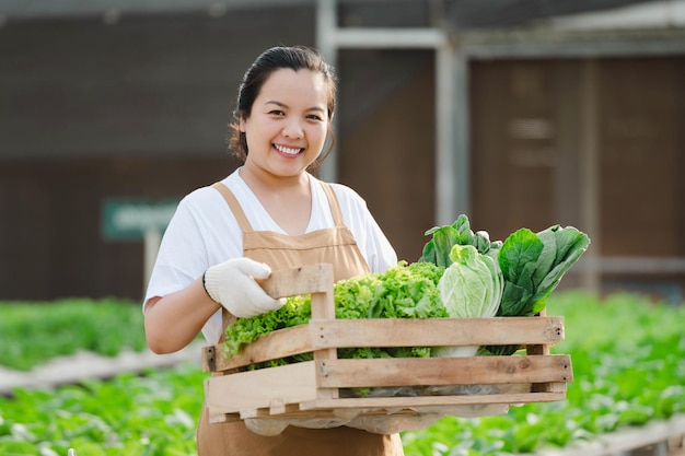 Portret van een Aziatische boerenvrouw met een houten kist vol verse rauwe groenten. Biologisch boerderijconcept.