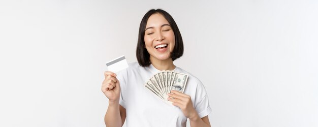 Portret van een aziatische vrouw die lacht met een creditcard en geld in contanten die in een t-shirt staat over w