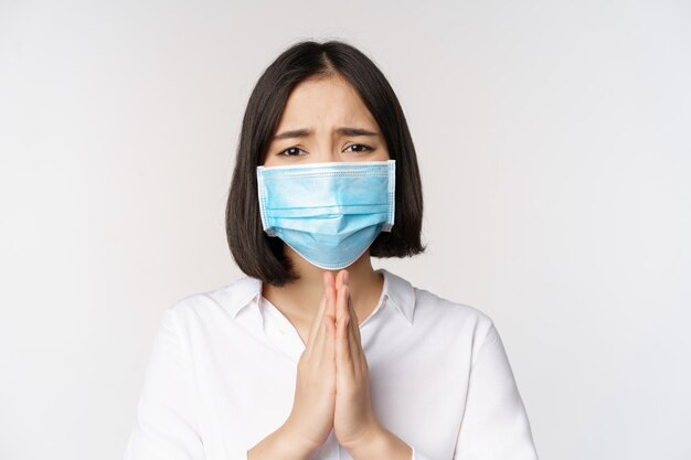 Portret van een aziatische vrouw met een medisch gezichtsmasker van covid die om hulp vraagt, zeg alsjeblieft dat je op een witte achtergrond staat