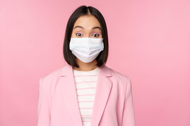 Portret van een Aziatische zakenvrouw met een medisch gezichtsmasker die een pakconcept van kantoorwerk draagt tijdens een pandemie van covid19 die over een roze achtergrond staat