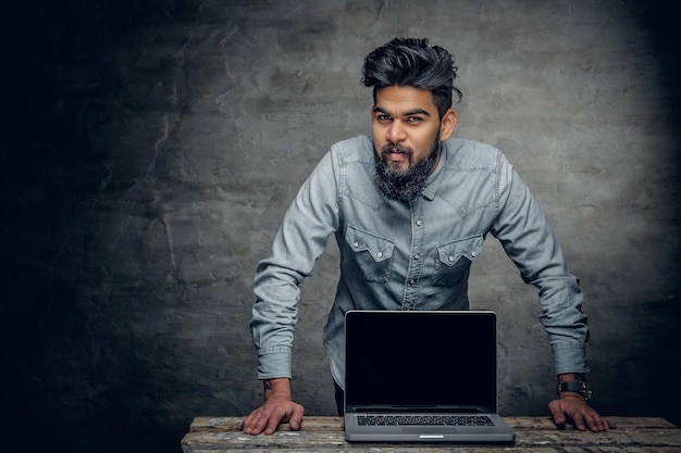 Portret van een bebaarde indiaan bij de tafel met een laptop erop.