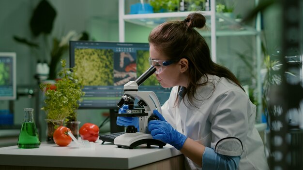 Portret van een bioloog-wetenschapper in witte jas die werkt in een expertiselaboratorium en onderzoekt naar een microscoop die biologisch ggo-blad analyseert