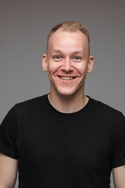 Portret van een blanke man in zwart t-shirt en een glimlach geïsoleerd op een grijze muur