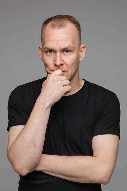 Portret van een blanke man in zwart t-shirt en houdt zijn hand in de buurt van het gezicht geïsoleerd op een grijze muur