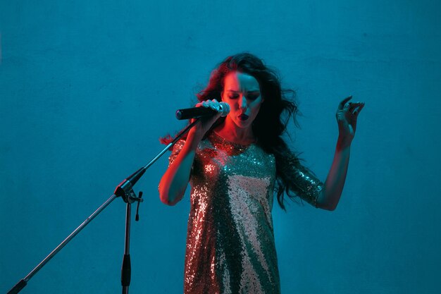 Portret van een blanke zangeres geïsoleerd op blauw in neonlicht