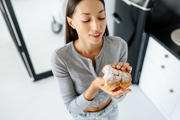 Portret van een blije vrouw eet thuis smakelijke croissants. Ongezond voedselconcept.
