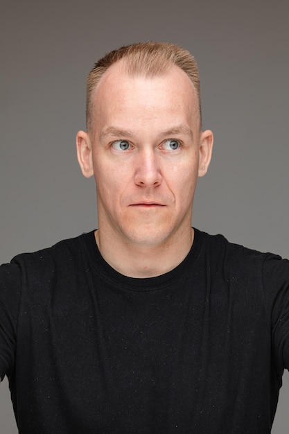 Portret van een blonde blanke man in een zwart t-shirt die wegkijkt met zijn ogen wijd open en verrast of geschokt.