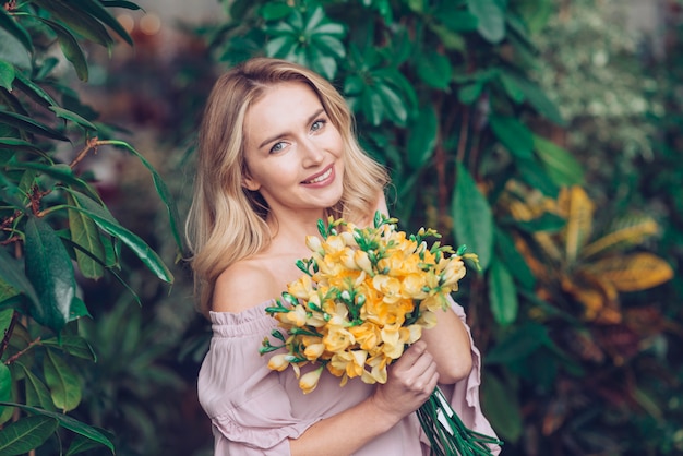 Portret van een blonde jonge vrouw die geel bloemboeket houdt