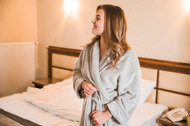 Portret van een blonde jonge vrouw die haar badjas vastbindt die zich in de slaapkamer bevindt