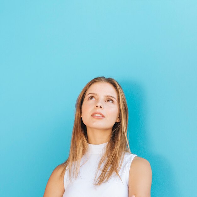 Portret van een blonde jonge vrouw die omhoog tegen blauwe achtergrond kijkt