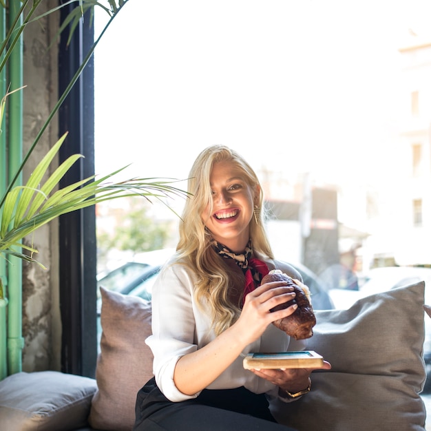 Portret van een blonde jonge vrouw die sandwich in caf� eet