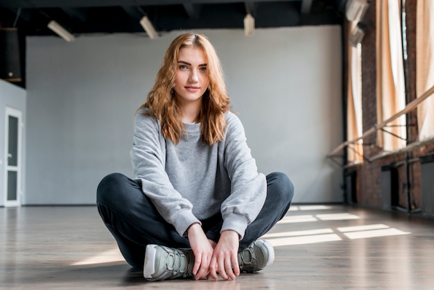 Portret van een blonde jonge vrouw zittend op de vloer in de studio