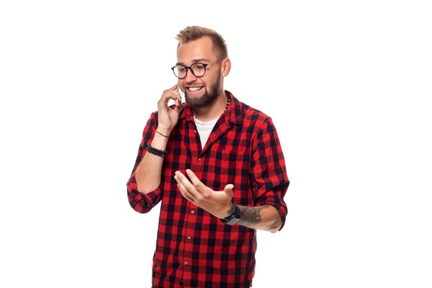 Portret van een casual jonge man die aan de telefoon spreekt en glimlacht terwijl hij wegkijkt, ergens omhoog. Studio opname. Jonge hipster man in geruit hemd en bril dragen op witte achtergrond