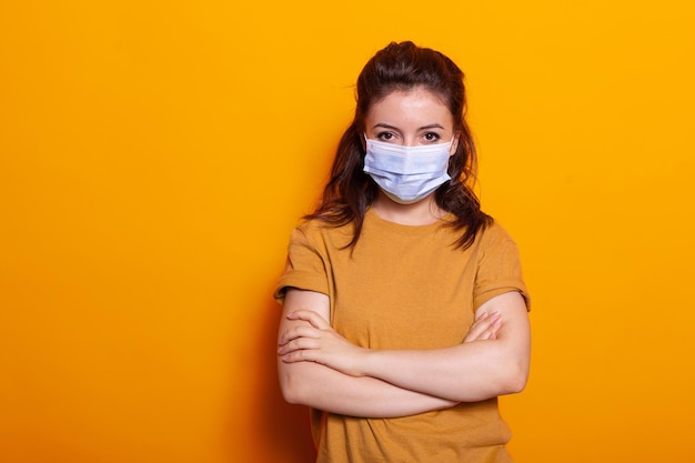 Portret van een casual vrouw met een gezichtsmasker tegen het virus, kijkend naar de camera in de studio. Jongere met bescherming en veiligheid, staande met gekruiste armen tijdens de pandemie van het coronavirus.