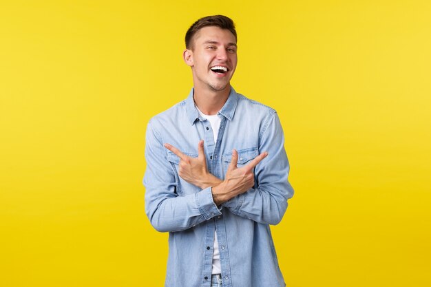 Portret van een charismatische knappe blonde man die blij lacht en met de vingers zijwaarts wijst, links en rechts varianten of producten laat zien, vrolijk over een gele achtergrond.